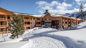 Ein mehrstöckiges Chalet mit Balkonen, ein Ski-Hang im Hintergrund und verschneite Umgebung.