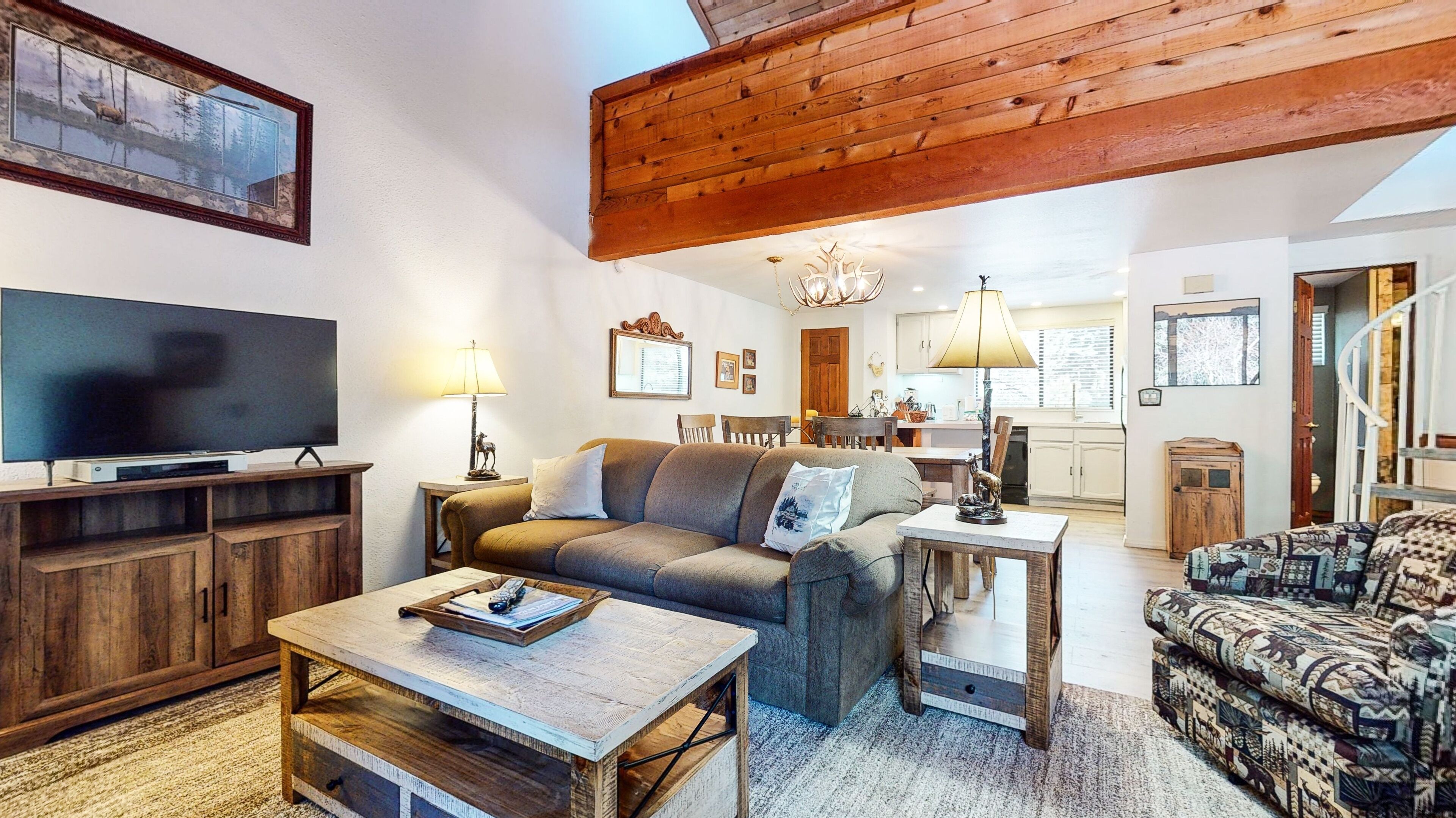 Una sala de estar acogedora con televisor, sofás, una mesa de centro y un comedor con lámpara.