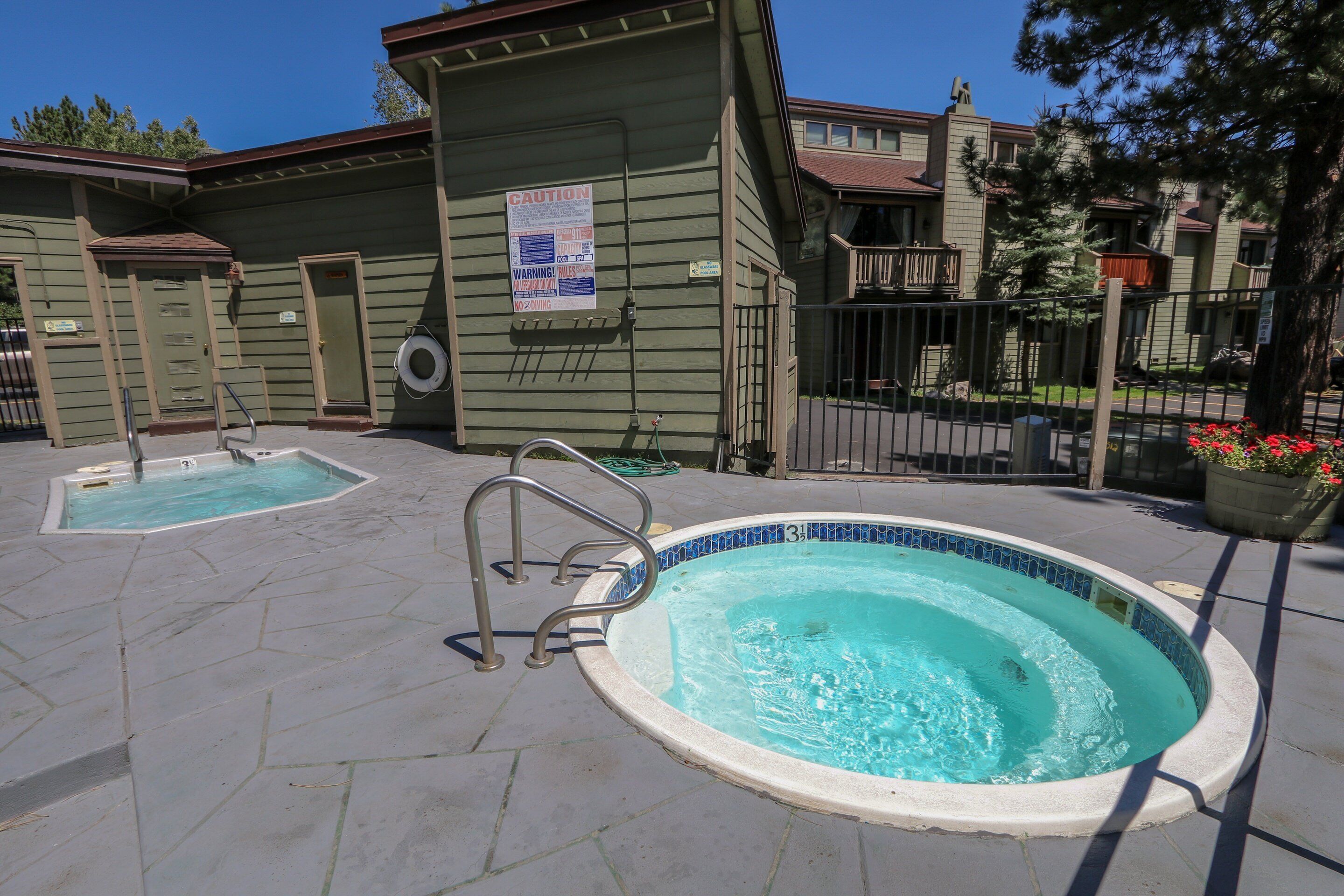 A pool area with two hot tubs and a safety sign on a building.
