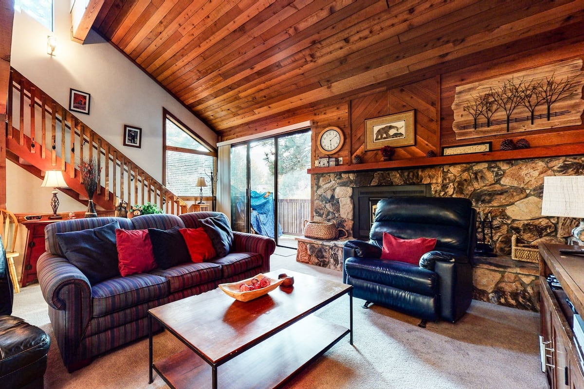 A cozy living room with a fireplace, a leather sofa, a coffee table, and a stone wall.