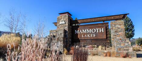 A sign for Mammoth Lakes with a stone and wood structure, surrounded by dry grass and shrubs.