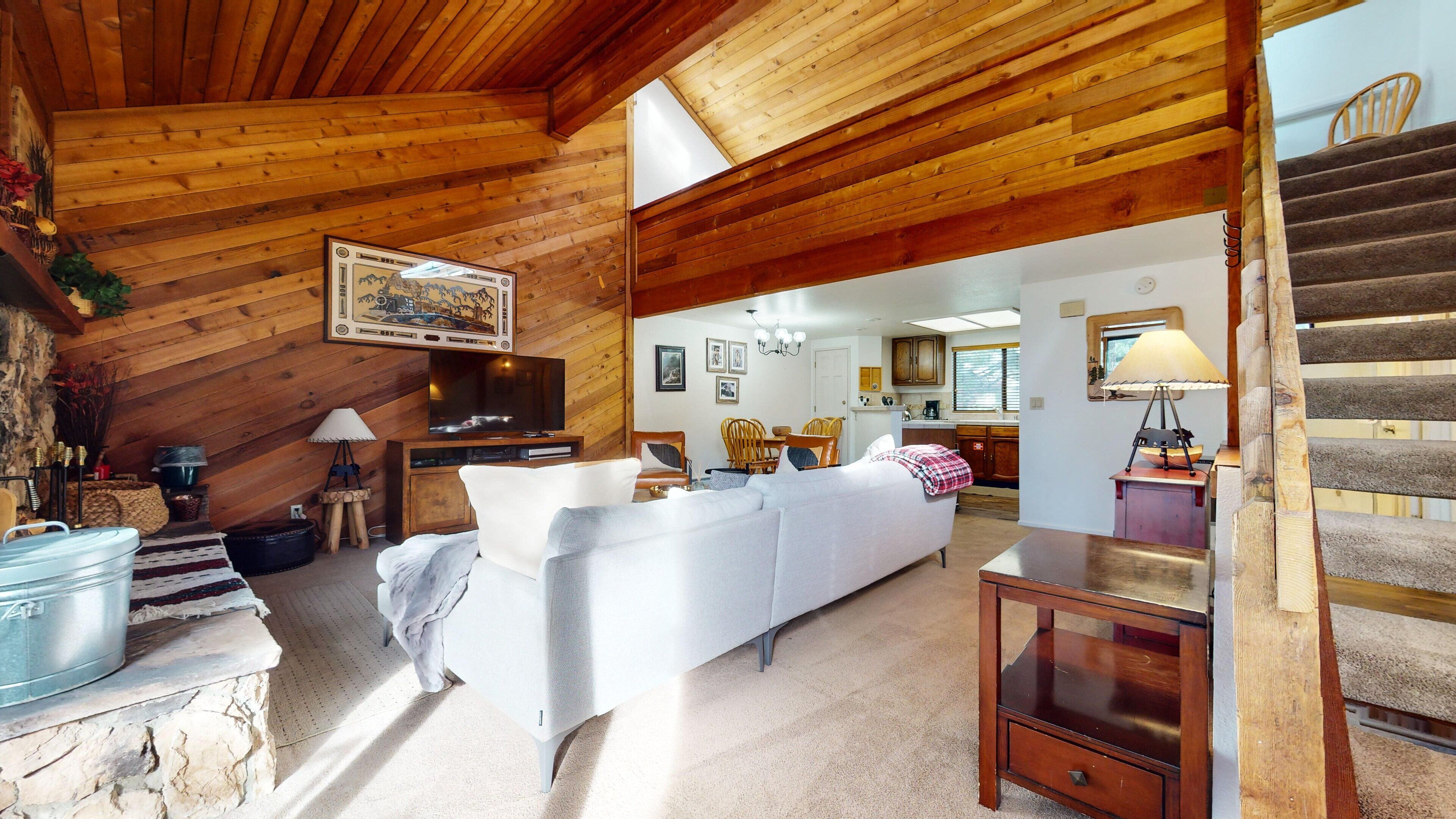 Ein gemütliches, rustikales Interieur mit Holzbalkendecke, einer Couch, einem Essbereich und einer Treppe.