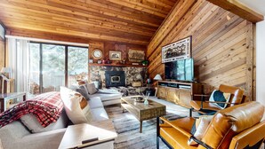 A cozy living room with a stone fireplace, wooden ceiling, and a large TV. - Mammoth Sierra Townhome (Mammoth Lakes)