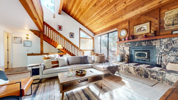 A cozy living room with a stone fireplace, wooden ceiling, and a staircase leading upstairs. - Mammoth Sierra Townhome (Mammoth Lakes)