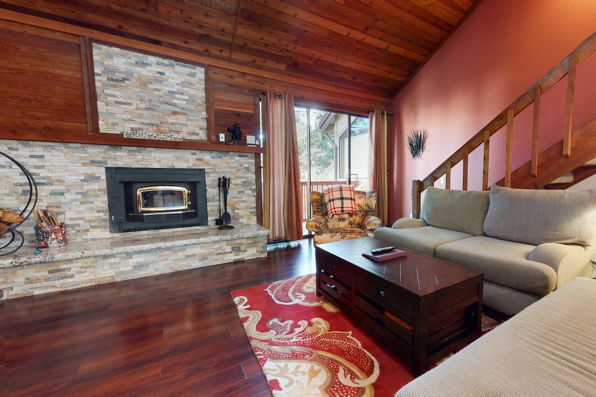 A cozy living room with a fireplace, wooden flooring, a sofa, a coffee table, and a staircase.