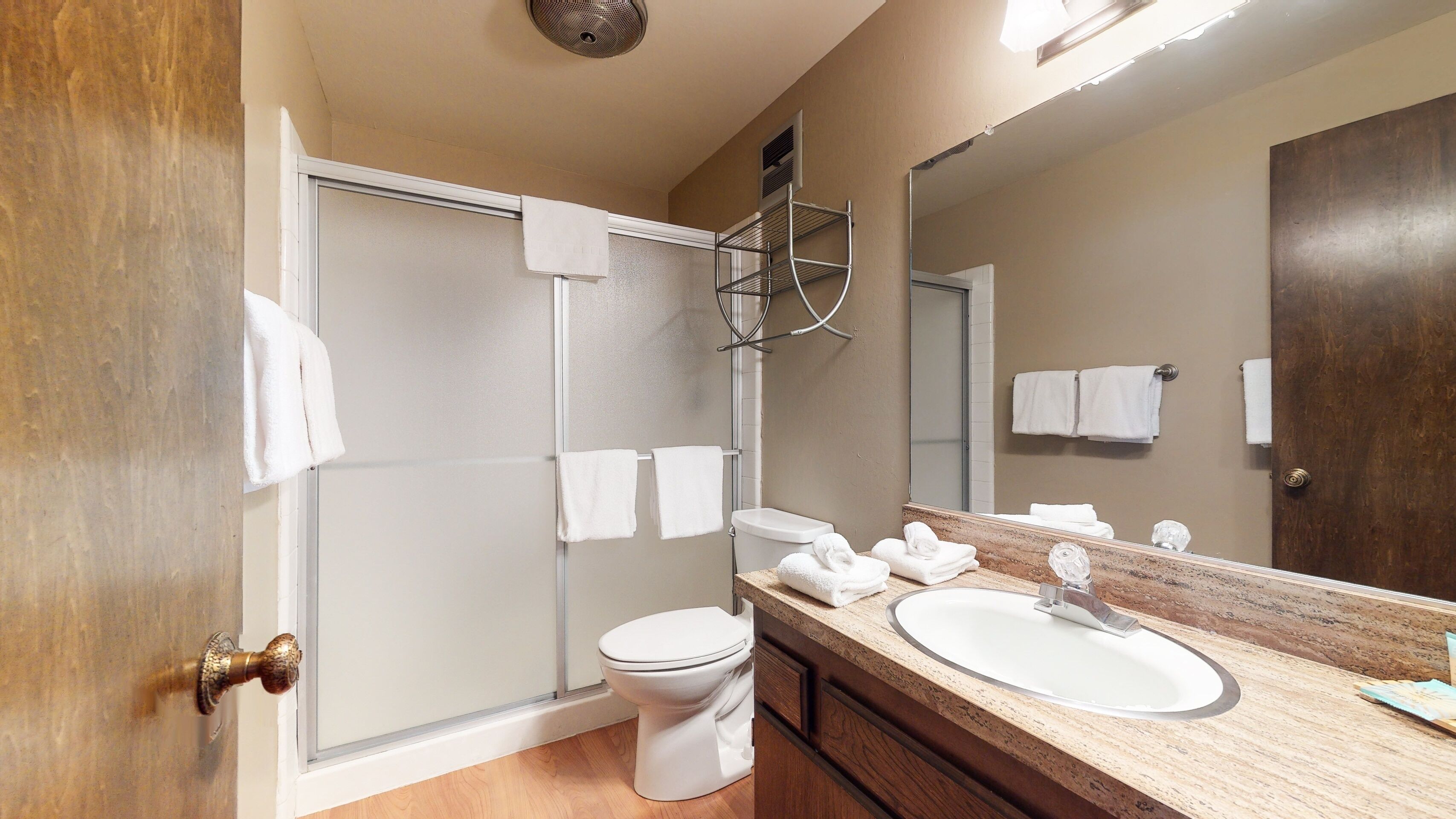 A bathroom with a shower, toilet, sink, and a large mirror.