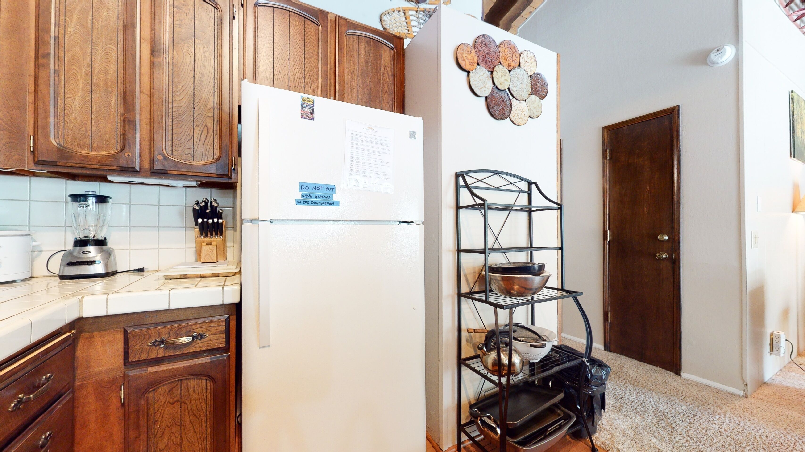 A kitchen with wooden cabinets, a white refrigerator, a blender, and a metal rack with pots and pans.
