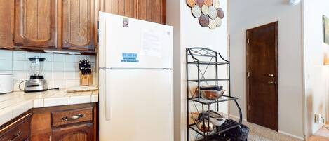 A kitchen with wooden cabinets, a white refrigerator, a blender, and a metal rack with pots and pans.
