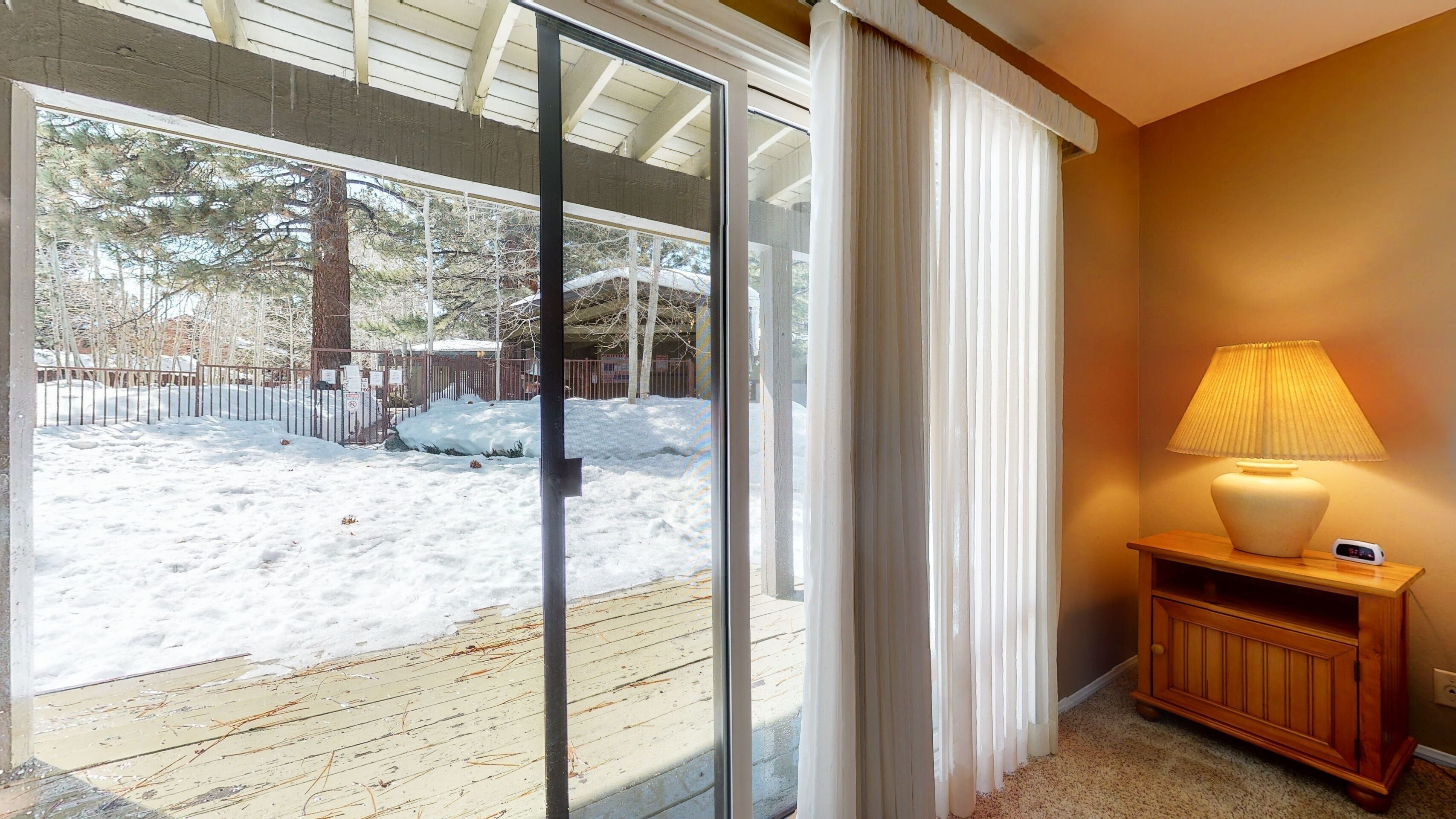 A room with a sliding glass door leading to a snowy outdoor area, a wooden bench with a lamp, and a wall clock.