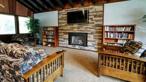 A living room with a stone fireplace, a flat-screen TV mounted above it, and two bookshelves filled with books. - Mammoth West 111 Cozy Condo, Just A Short Walk to Canyon Lodge by RedAwning (Mammoth Lakes)