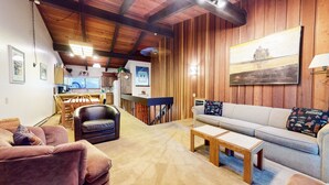A cozy living room with a sofa, armchair, and coffee table, wooden panel walls, and a kitchen in the background. - Mammoth West 111 Cozy Condo, Just A Short Walk to Canyon Lodge by RedAwning (Mammoth Lakes)