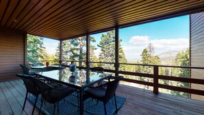 A wooden deck with a glass table and chairs, overlooking a forested landscape with mountains. - Bridges Townhome 13 Mountain View Townhome just Steps to the Slopes with Private Garage and Washer Dryer by RedAwning (Mammoth Lakes)