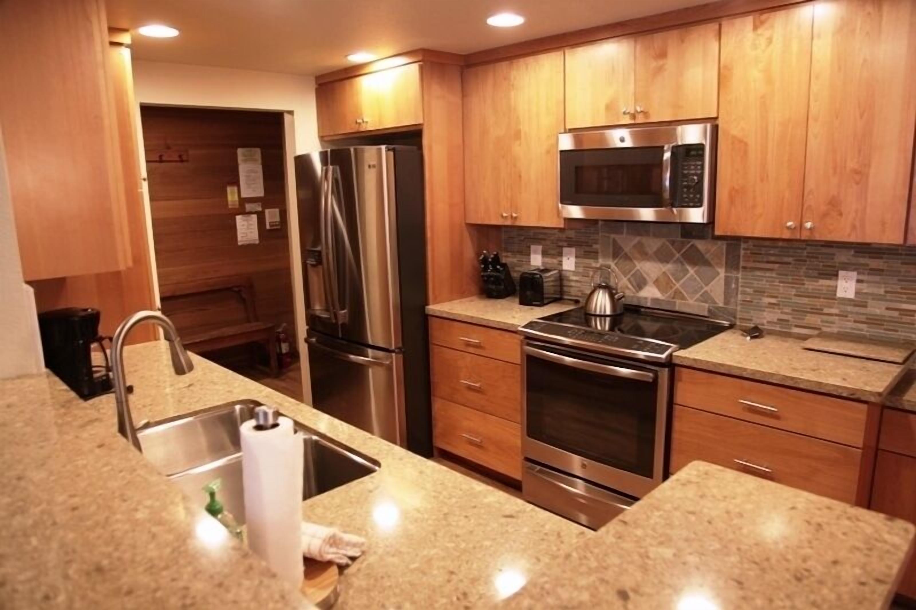 A modern kitchen with wooden cabinets, stainless steel appliances, granite countertops, and a tiled backsplash.