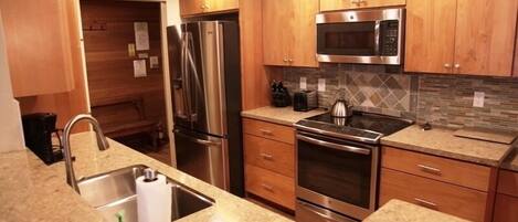 A modern kitchen with wooden cabinets, stainless steel appliances, granite countertops, and a tiled backsplash.