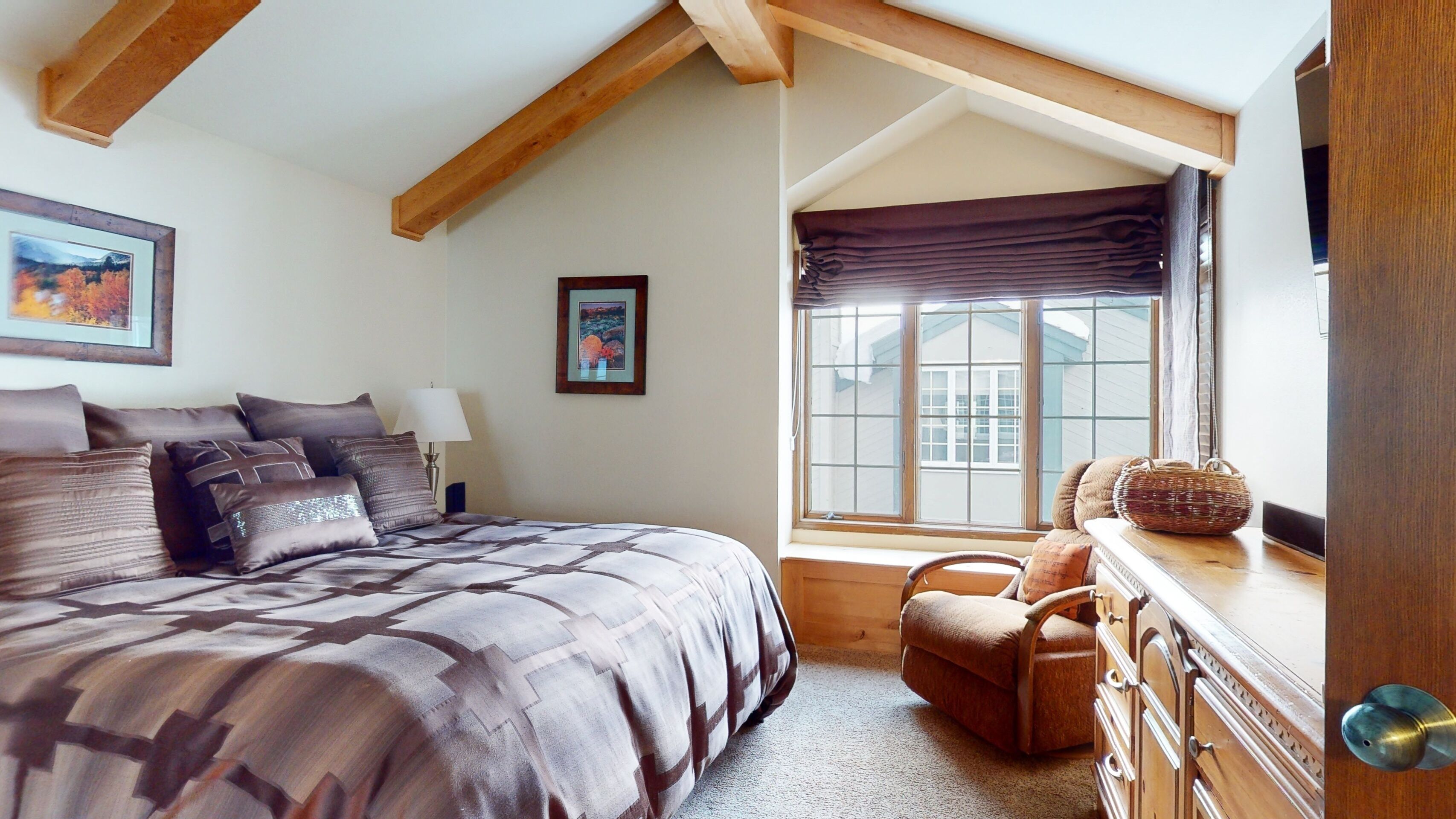 A bedroom with a large bed, a chair, a dresser, and a window with a view of a house.