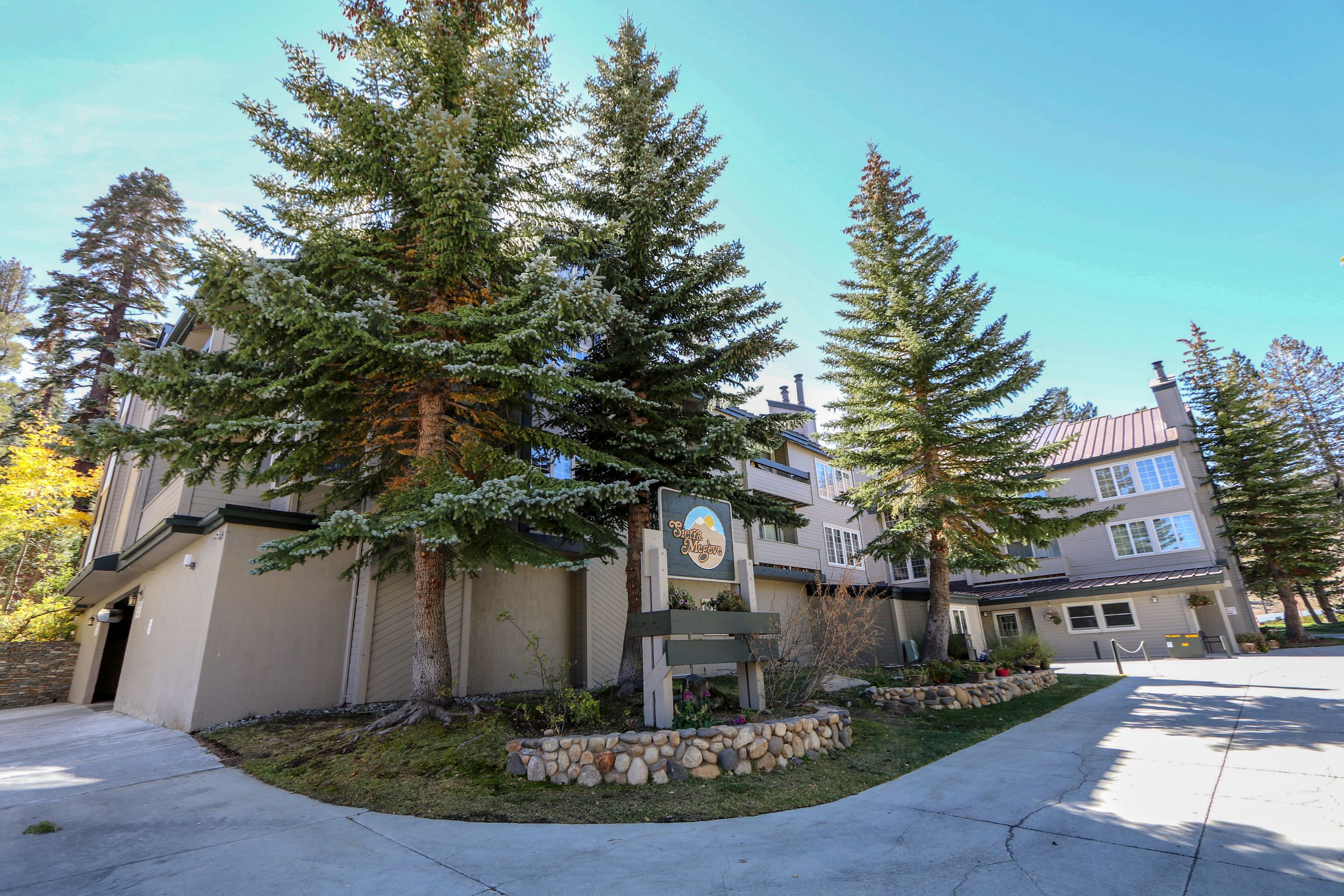 A two-story building with a stone facade, large windows, and a landscaped front yard with trees and a stone border.