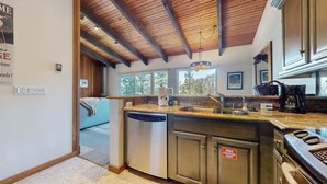 A modern kitchen with a wooden ceiling, a built-in dishwasher, a stainless steel sink, and a stove.