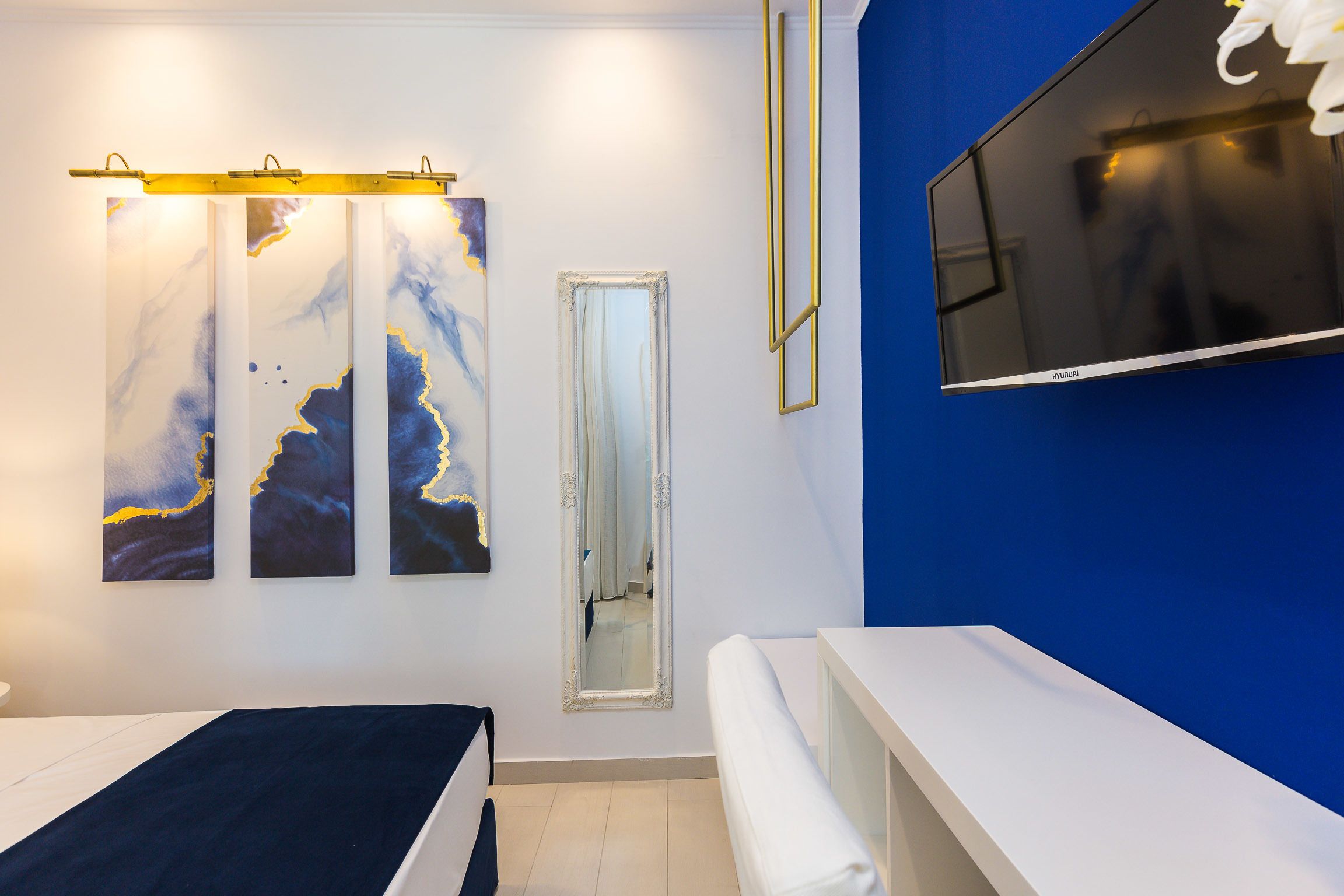A modern hotel room with a bed, a bench, a large mirror, and artwork on the wall.