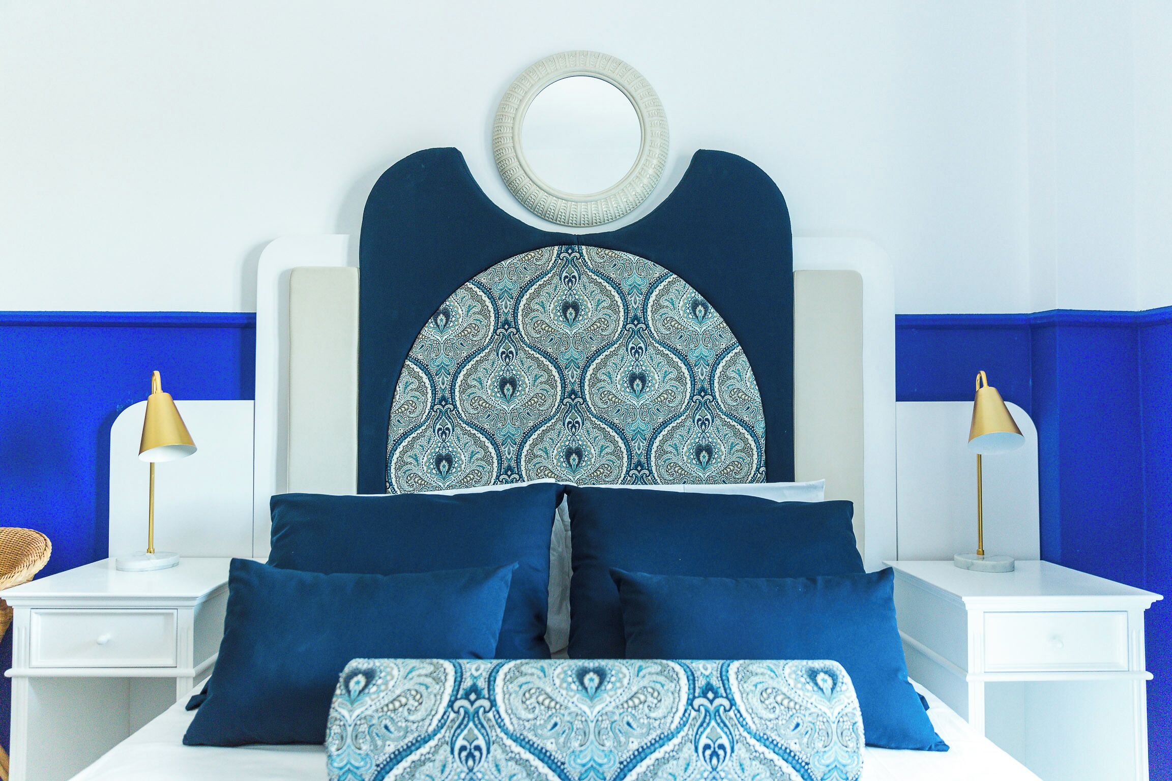 Un lit avec une tête de lit à motifs, deux tables de chevet avec des lampes et un mur bleu.