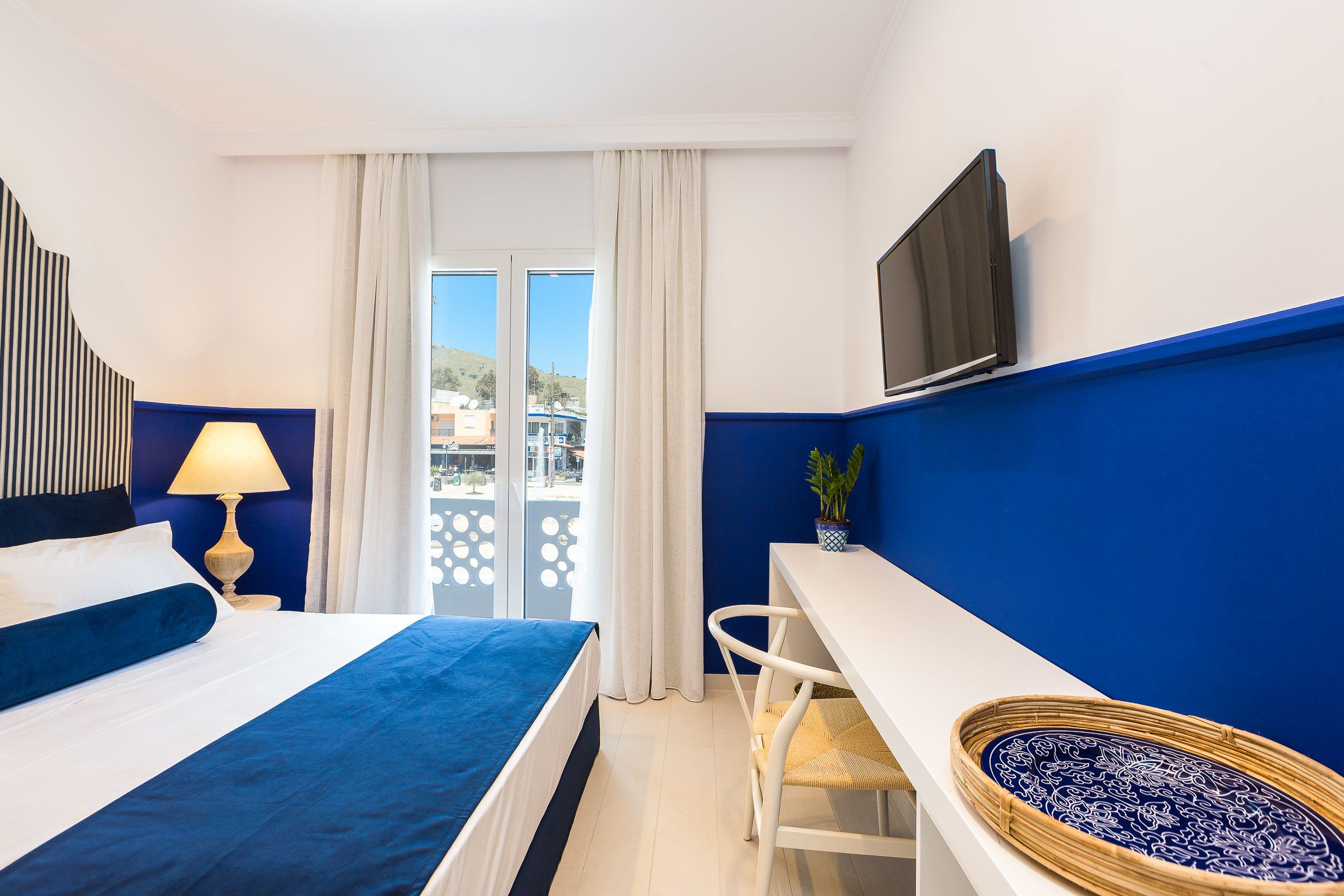 Habitación de hotel con cama, escritorio, televisión y vista al exterior.
