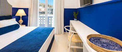 A hotel room with a bed, a desk, a TV, and a view of the outside.