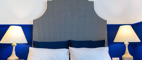 A bed with white and blue bedding, flanked by two bedside tables with lamps, against a wall with a striped pattern.