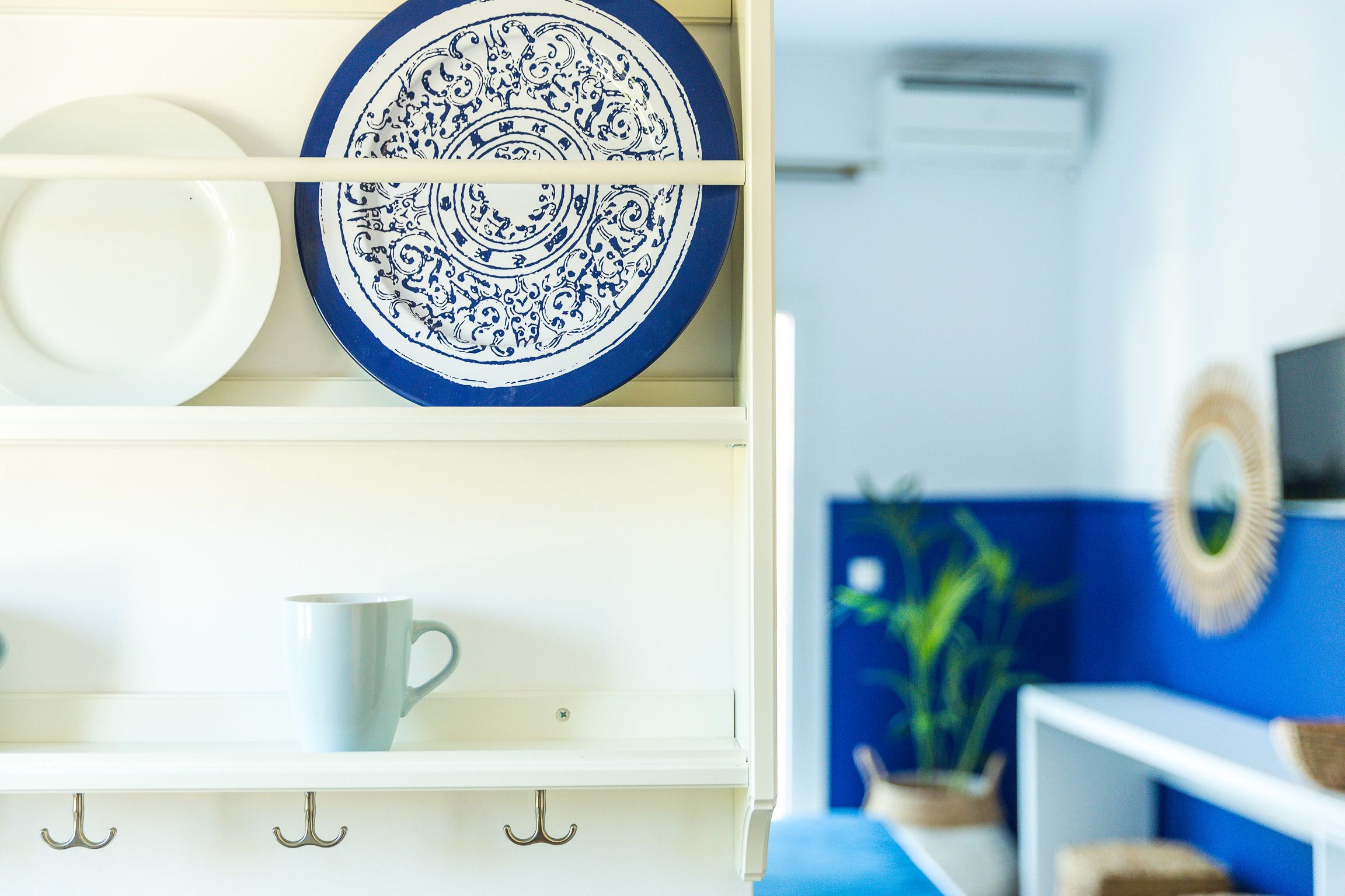 A kitchen with white cabinets, a blue and white plate, and a white mug on the counter.