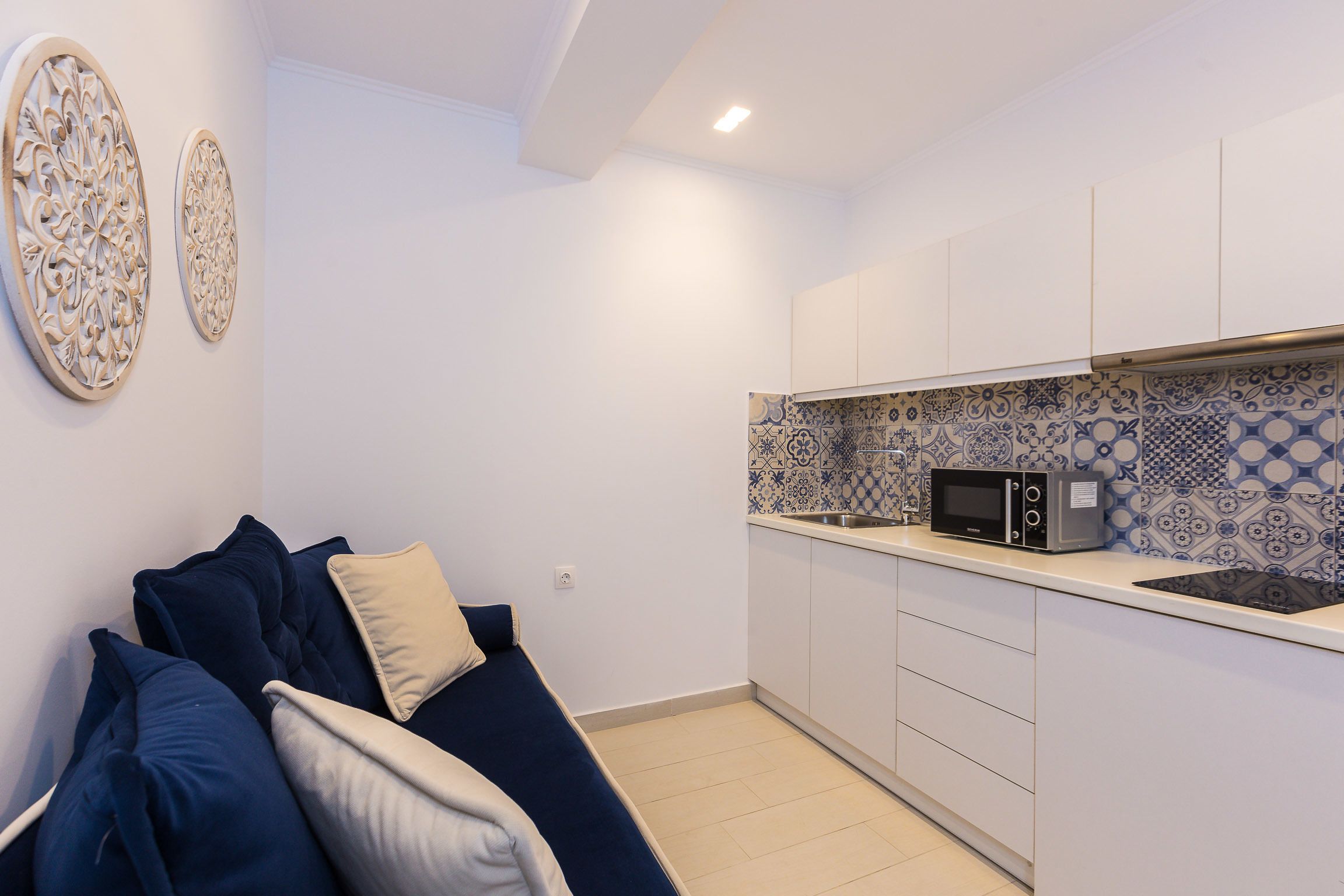 Una cocina pequeña con armarios blancos, un microondas y azulejos decorativos en la pared.