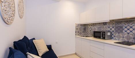 Una cocina pequeña con armarios blancos, un microondas y azulejos decorativos en la pared.