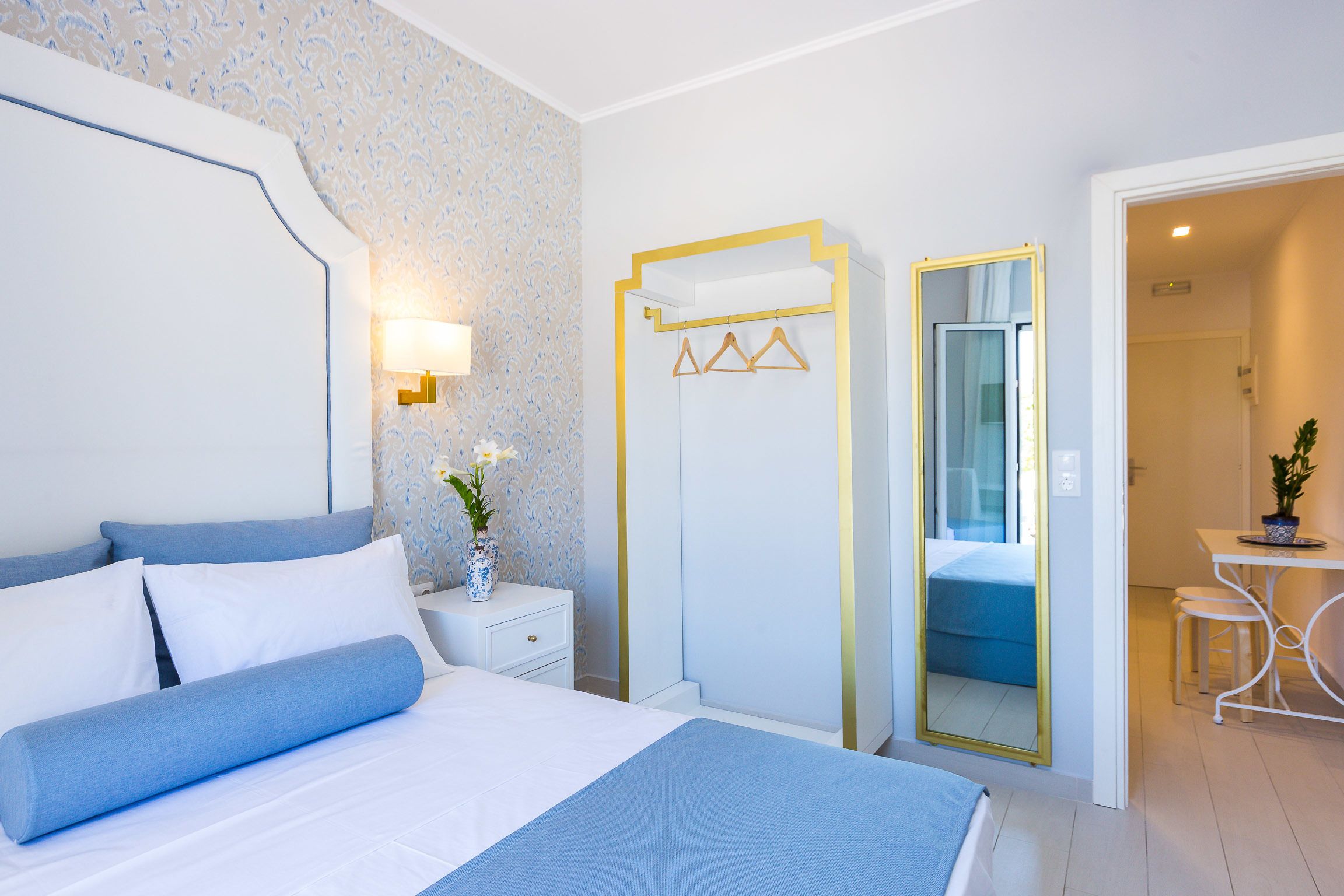 A bedroom with a bed, bedside table, lamp, and a mirror.