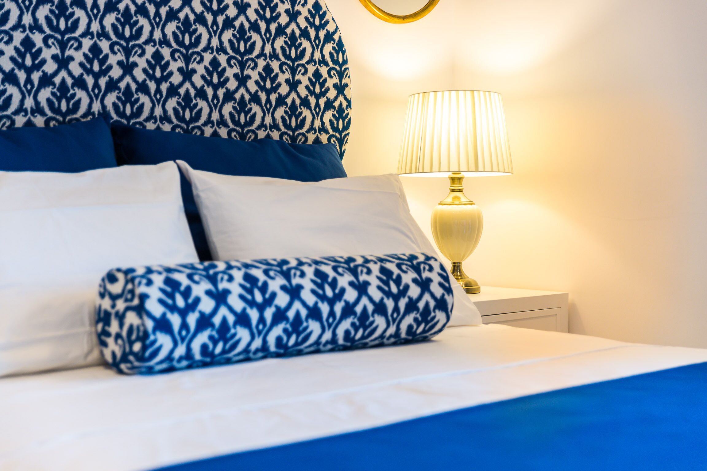 Un letto rifatto con cuscini a motivi blu e bianchi, una lampada da comodino e una parete con decorazioni.