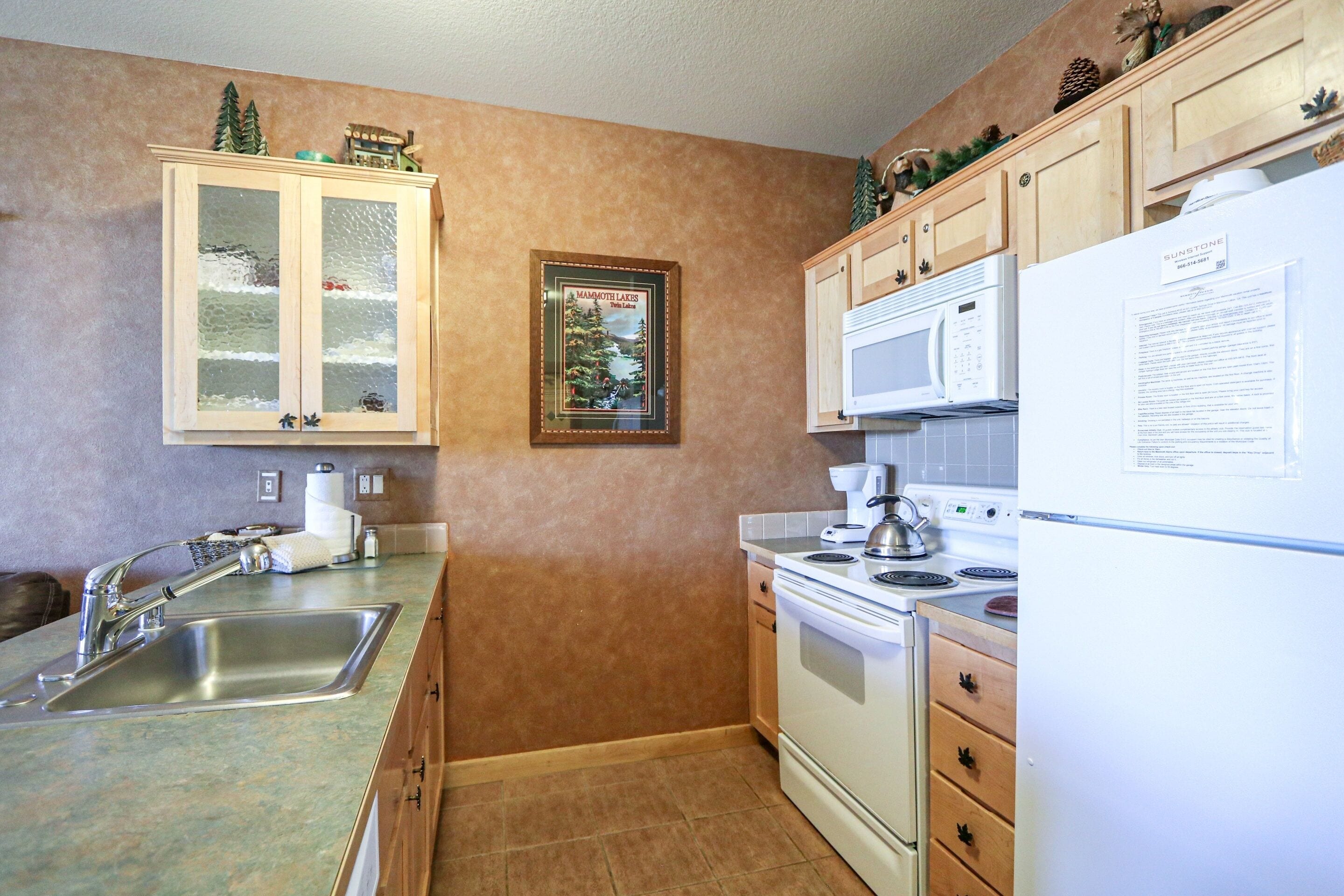A kitchen with a stainless steel sink, wooden cabinets, a white stove, and a refrigerator.