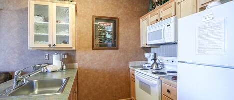 A kitchen with a stainless steel sink, wooden cabinets, a white stove, and a refrigerator.