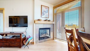 A living room with a fireplace, a television, and a dining area with wooden furniture. - Sunstone 103 Updated Condo At Sunstone Lodge with Great Complex Amenities, near Ski-In Ski-Out by RedAwning (Mammoth Lakes)