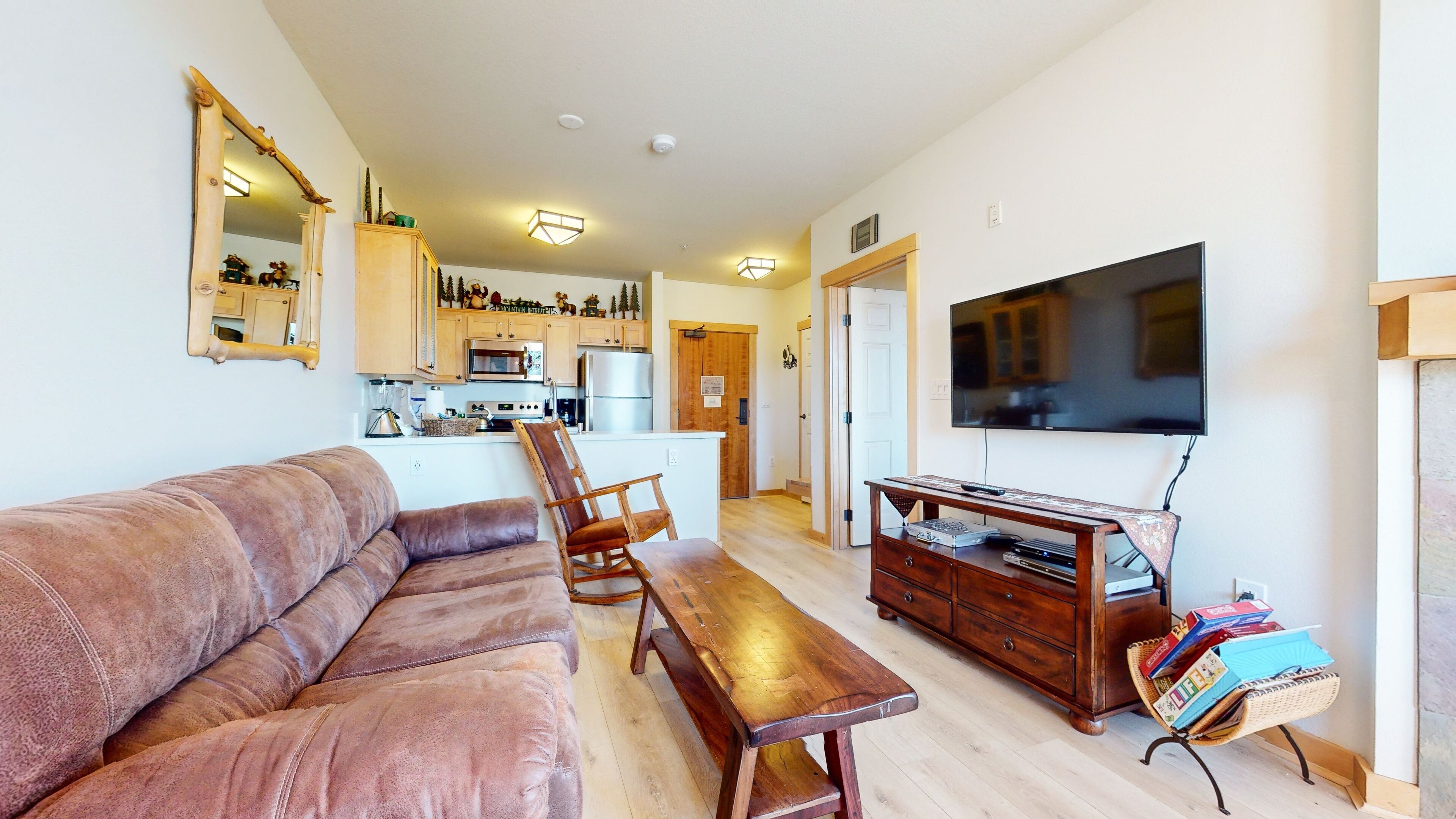 A living room with a brown leather sofa, wooden coffee table, and a TV stand with electronic devices.