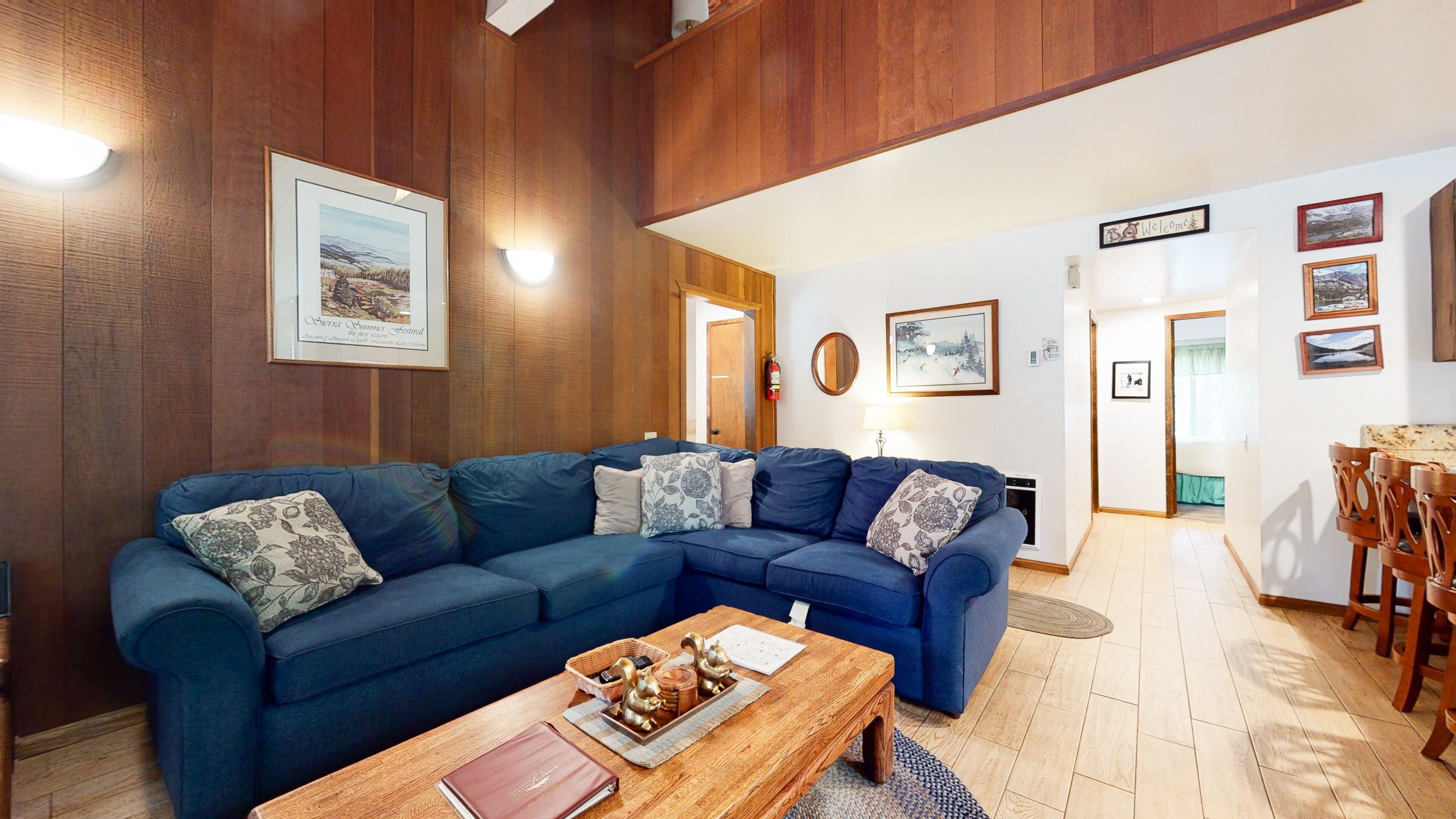 A living room with a blue sectional sofa, a wooden coffee table with decorative items, and a dining area with wooden chairs and a table.