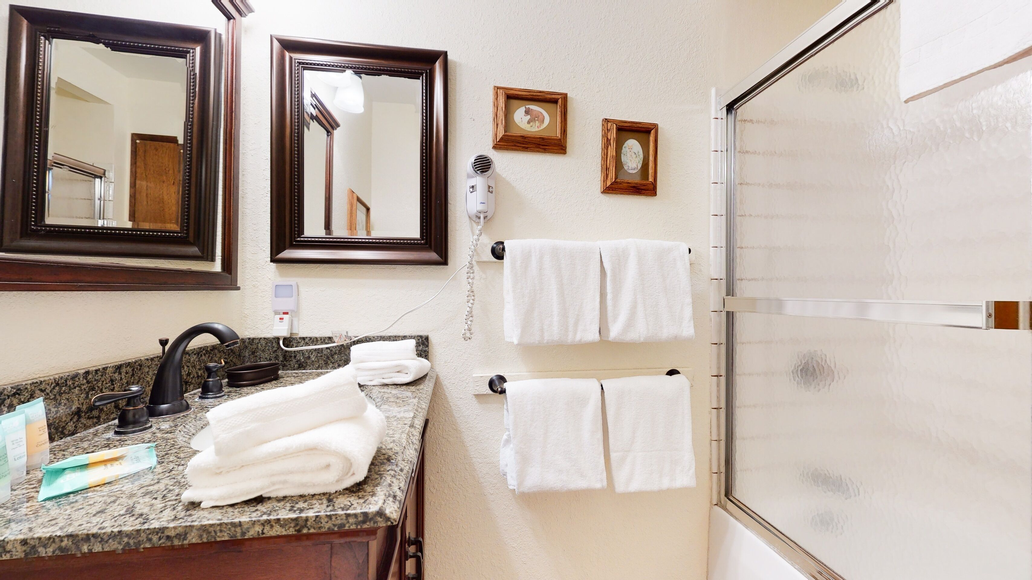 A bathroom with a granite countertop, a black faucet, two framed mirrors, and two towels hanging on hooks.