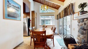 A spacious kitchen with a dining table, wooden chairs, a refrigerator, and a stone fireplace. - Horizons 4 188 Cozy Condo with Great Complex Amenities, On the Shuttle Route by RedAwning (Mammoth Lakes)