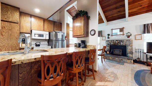 A kitchen with wooden cabinets, a granite countertop, a stove, a microwave, and a refrigerator. There are four wooden chairs at the bar. - Horizons 4 188 Cozy Condo with Great Complex Amenities, On the Shuttle Route by RedAwning (Mammoth Lakes)