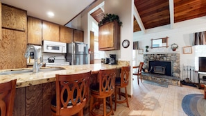 A modern kitchen with wooden cabinets, a granite countertop, stainless steel appliances, and a stone fireplace. - Horizons 4 188 Cozy Condo with Great Complex Amenities, On the Shuttle Route by RedAwning (Mammoth Lakes)