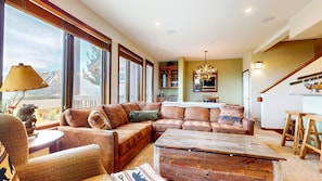 A spacious living room with a sectional sofa, a wooden coffee table, and a view of the mountains through large windows. - Eagle Run 212 Ski-in Ski-Out Luxury Mountain Cabin with Private Washer Dryer by RedAwning (Mammoth Lakes)