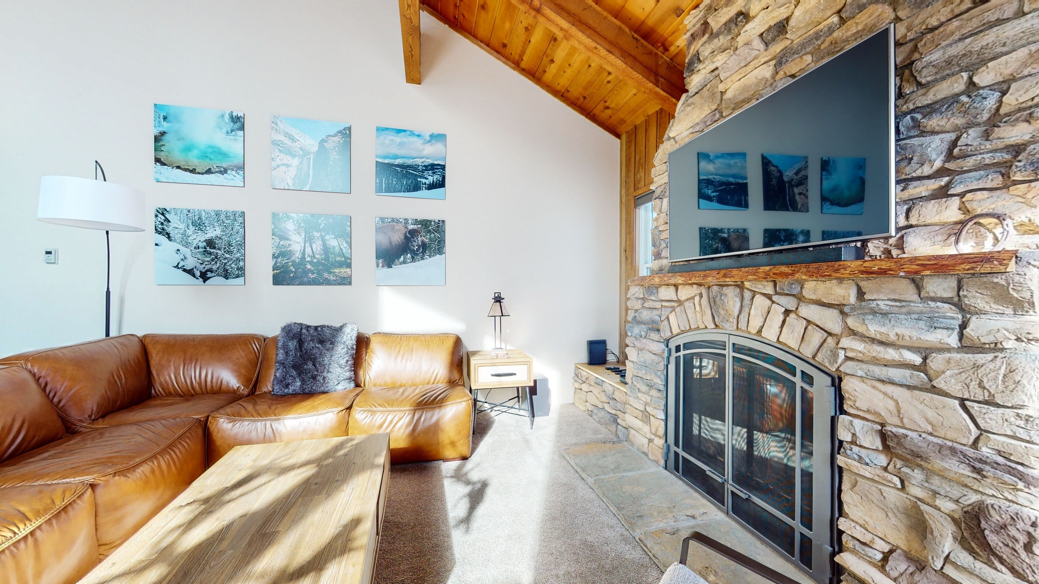 A living room with a stone fireplace, leather sofa, and wall-mounted artwork.