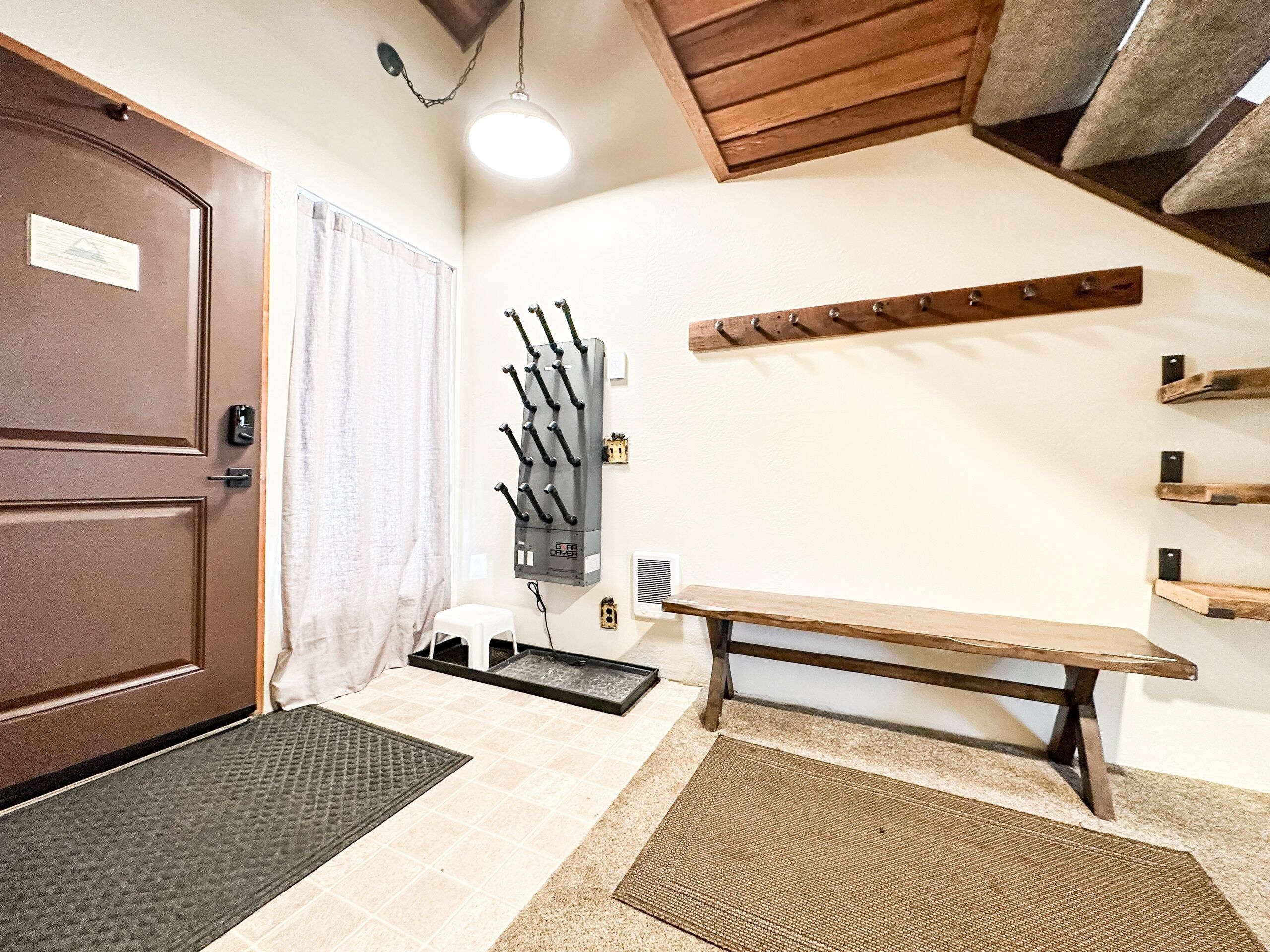 Quarto com porta marrom, cadeira branca, um banco, um porta-roupas e aquecedor fixado na parede.