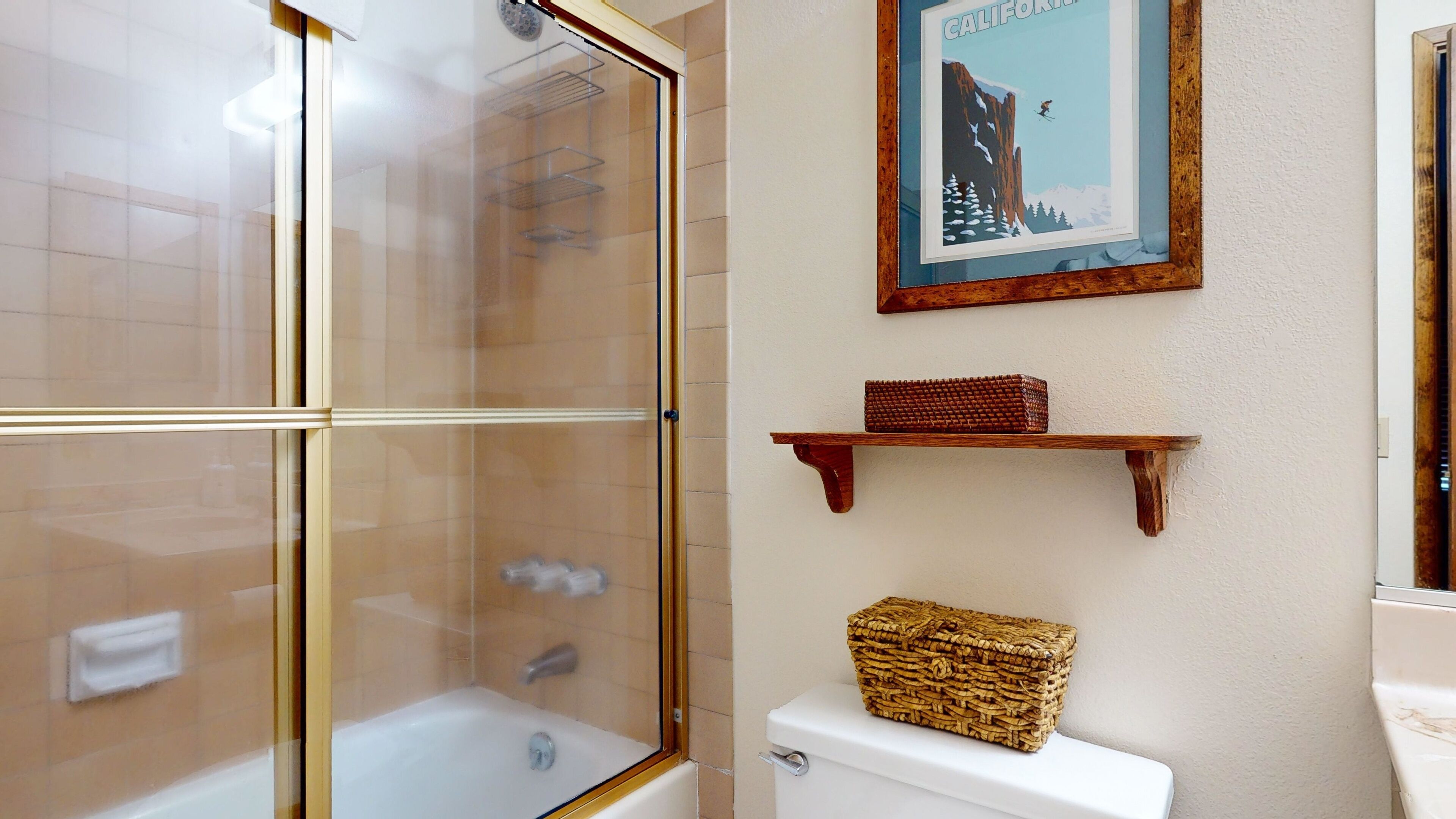 A bathroom with a glass shower enclosure, a framed picture on the wall, and a wooden shelf with a woven basket.