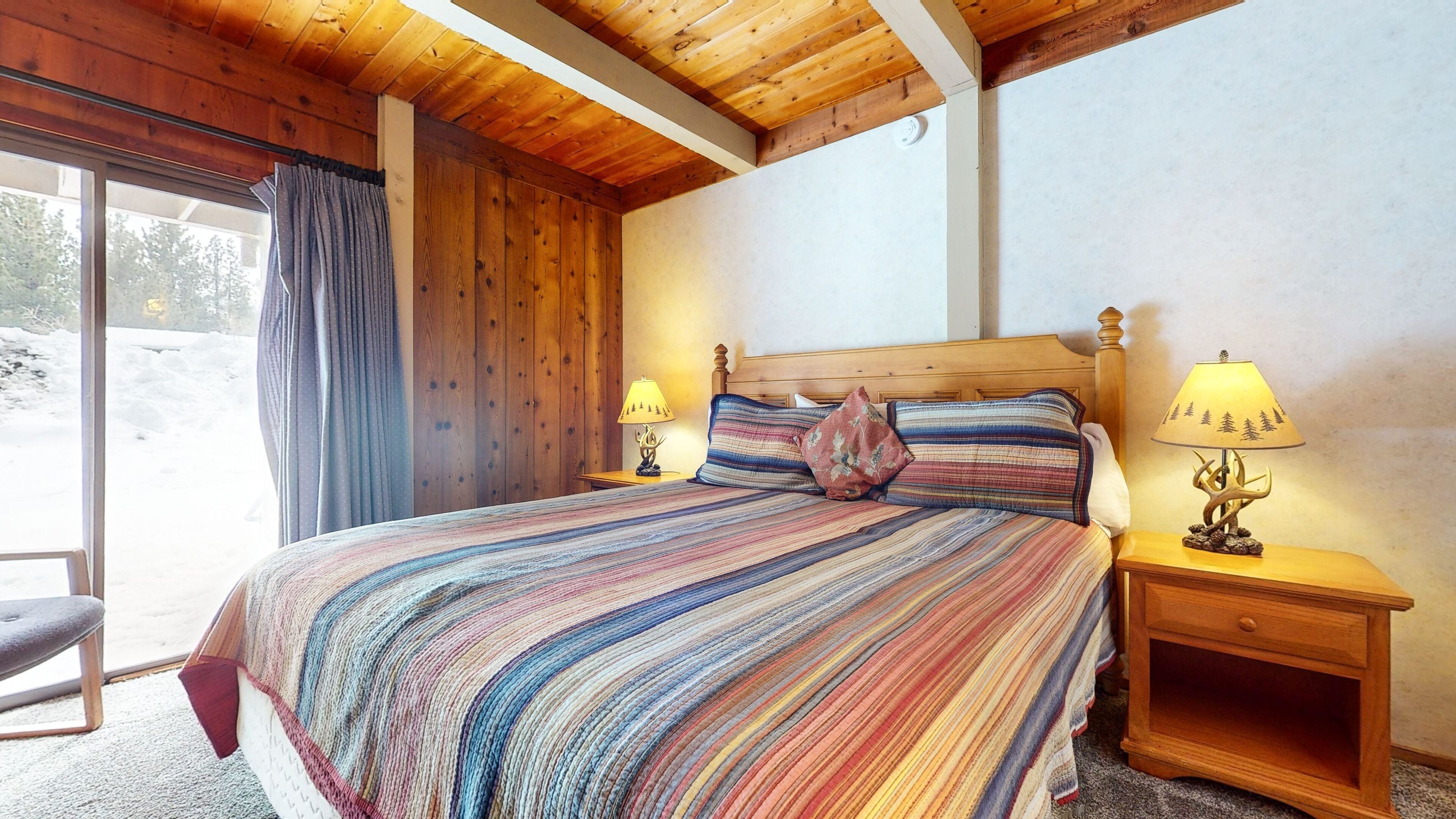 Een slaapkamer in een houten hut met een groot bed, twee bedlampen en uitzicht op een besneeerd landschap.