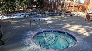 A hot tub with a tiled deck and a stone border, surrounded by a stone wall and a bench. - Juniper Springs Lodge 539 Deluxe Condo Great Complex Amenities near Ski-In Ski-Out by RedAwning (Mammoth Lakes)