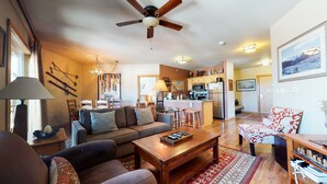 A cozy living room with a sofa, coffee table, and a dining area with chairs. A kitchen is visible in the background with a refrigerator and stove. - Juniper Springs Lodge 539 Deluxe Condo Great Complex Amenities near Ski-In Ski-Out by RedAwning (Mammoth Lakes)