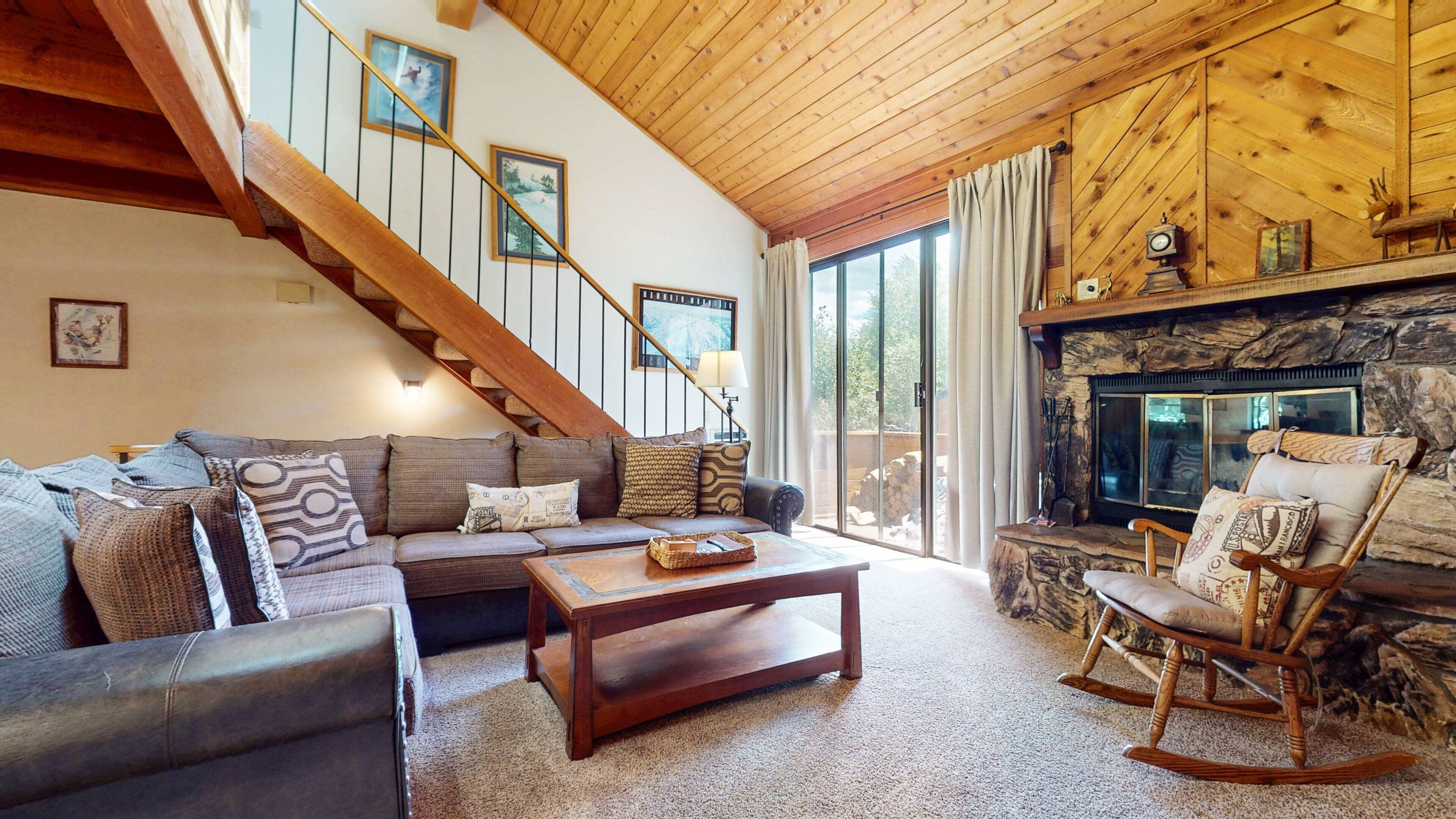 A cozy living room with a wooden staircase, a fireplace, and a large window.