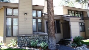 A two-story building with a stone foundation, a large tree in front, and an American flag on the right. - St. Moritz 12 Bright and cozy Mountain Cabin, Centrally Located by RedAwning (Mammoth Lakes)