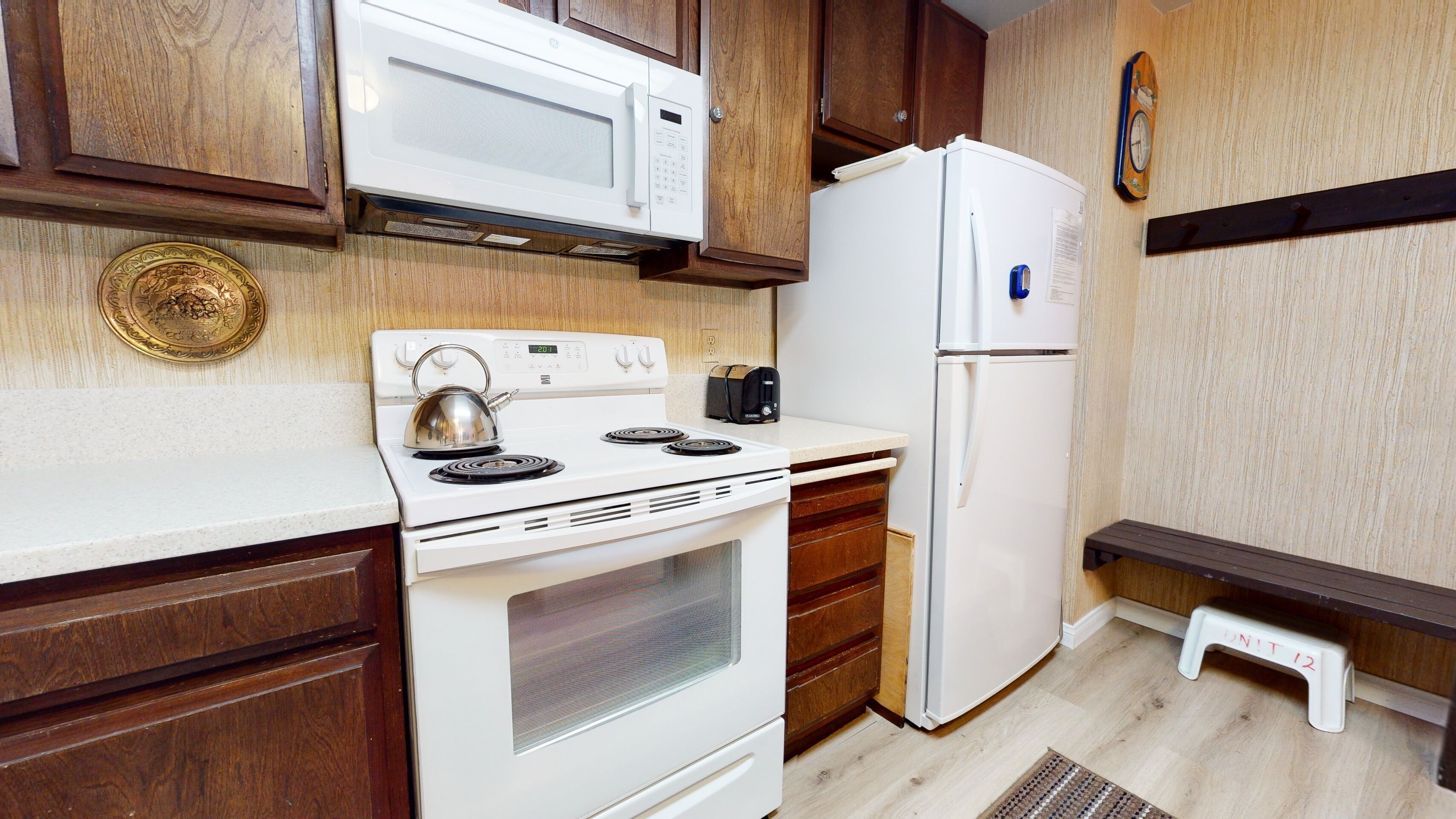 A compact kitchen with white appliances, wooden cabinets, and a small step stool.